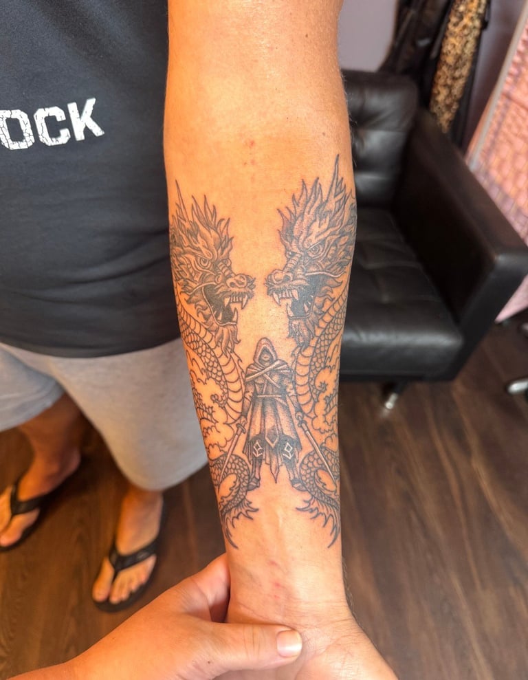 Detailed dragon tattoo on person's forearm featuring two symmetrical dragons facing each other with ornate scales and decorative elements