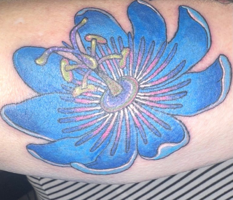 Blue and purple flower tattoo on skin with detailed center stamen and radiating petals