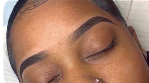 Close-up of womans face with eyes closed, showing defined eyebrows and glowing skin with natural makeup