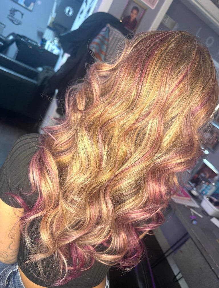 Rose gold lowlights hair color at CC Styling Studio in Bradenton, FL — long wavy hair with blonde, golden, and rose pink highlights and layers photographed from behind
