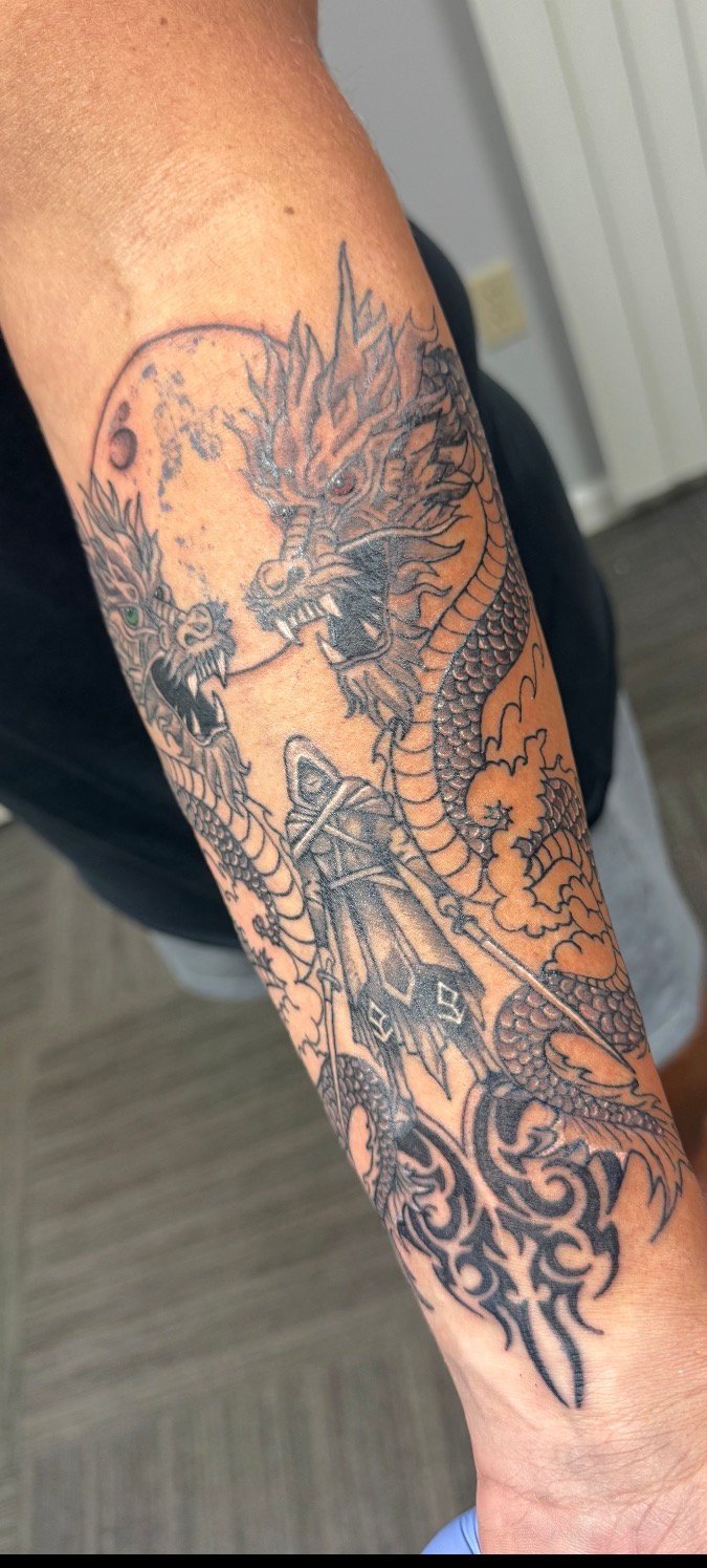 Detailed dragon tattoo on a person's forearm featuring intricate linework with moon and ornamental designs